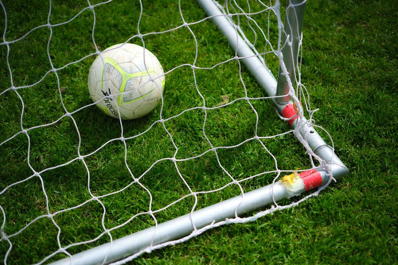 about-me Close-up image of a soccer ball resting in a goal net on a vibrant green grass field.